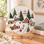 Snowy christmas village embroidery kit finished hoop displayed on a wooden stand as cozy tabletop decor