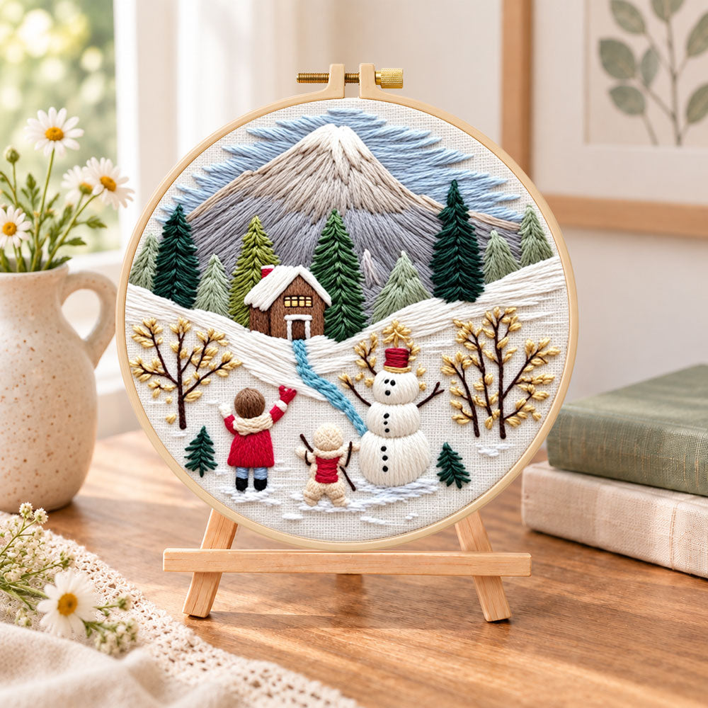 Snowy mountain holiday fun embroidery kit finished hoop displayed on a wooden stand as cozy tabletop decor