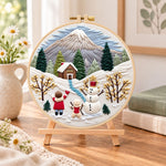 Snowy mountain holiday fun embroidery kit finished hoop displayed on a wooden stand as cozy tabletop decor