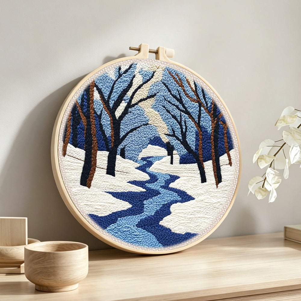 Snowy river landscape with bare trees punch needle artwork displayed on a table