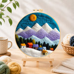 Finished snowy village under the mountains needle felting displayed on a wooden easel