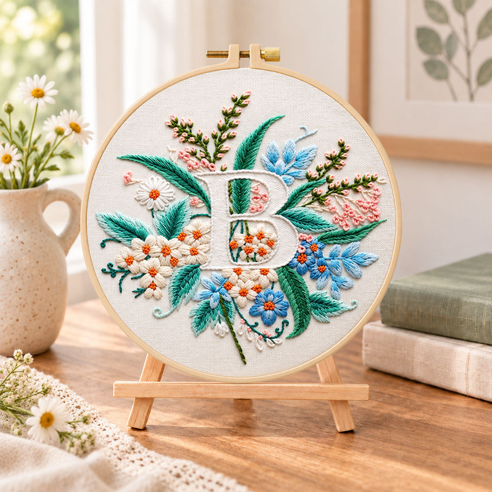 Soft pastel blooms and letter b embroidery kit finished hoop displayed on a wooden stand as cozy tabletop decor