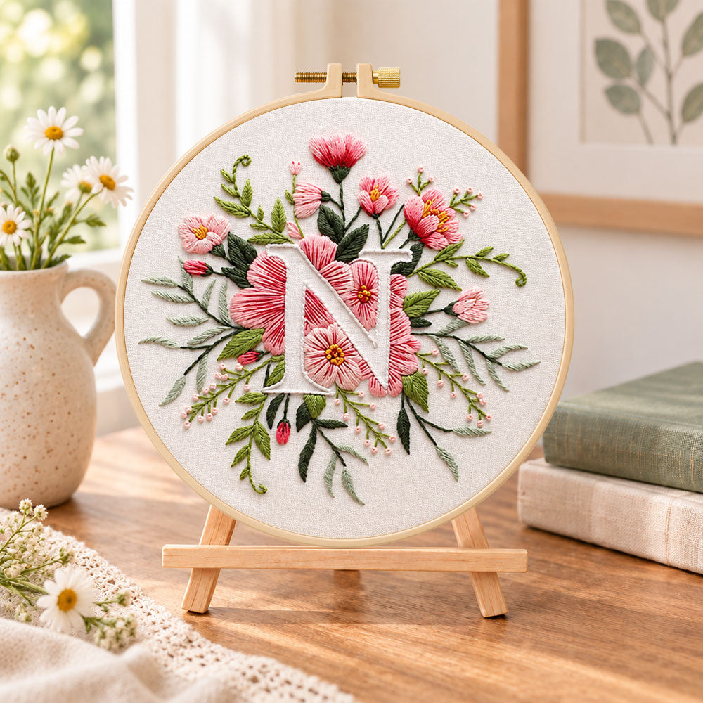 Soft pink petals and letter n embroidery kit finished hoop displayed on a wooden stand as cozy tabletop decor