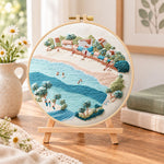 Soft seaside town embroidery kit finished hoop displayed on a wooden stand as cozy tabletop decor