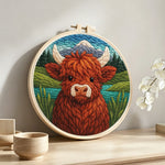 Springtime highland cow and mountain lake punch needle artwork displayed on a table