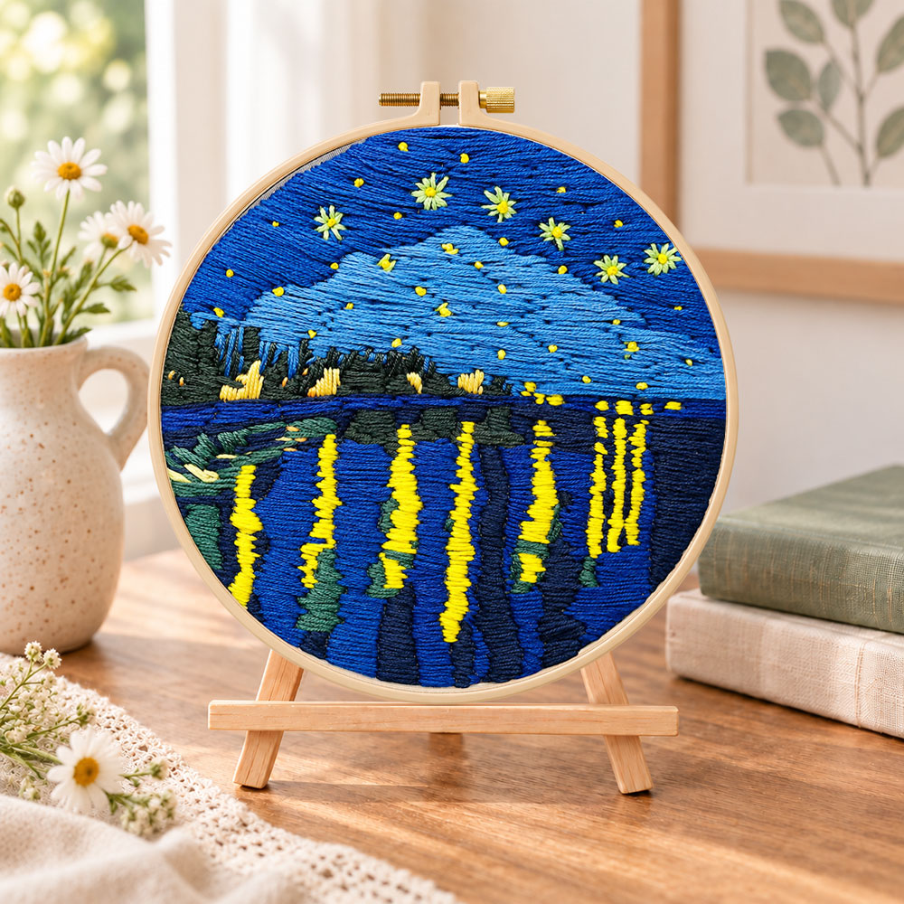 Starry night lakeside view embroidery kit finished hoop displayed on a wooden stand as cozy tabletop decor