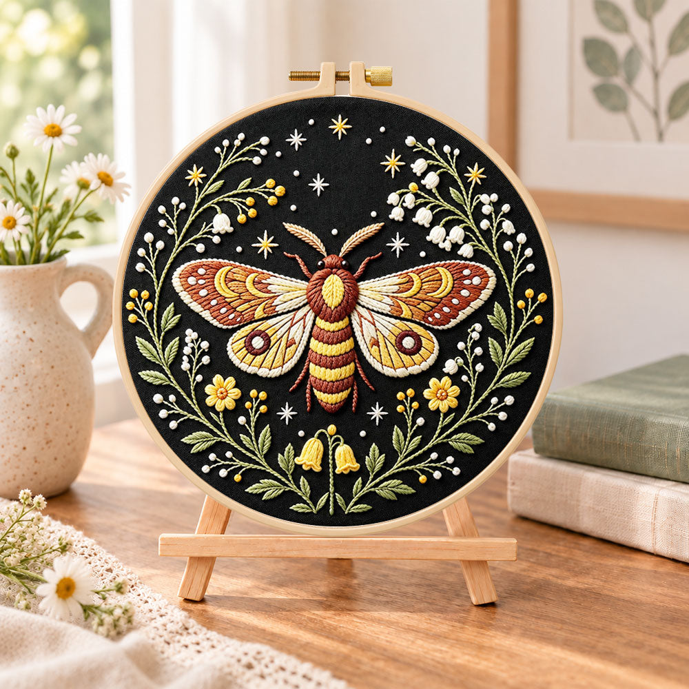 Starry night moth embroidery kit finished hoop displayed on a wooden stand as cozy tabletop decor