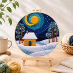 Finished swirling blue sky and yellow snowy cottage needle felting displayed on a wooden easel