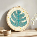Teal monstera leaf with stars punch needle artwork displayed on a table