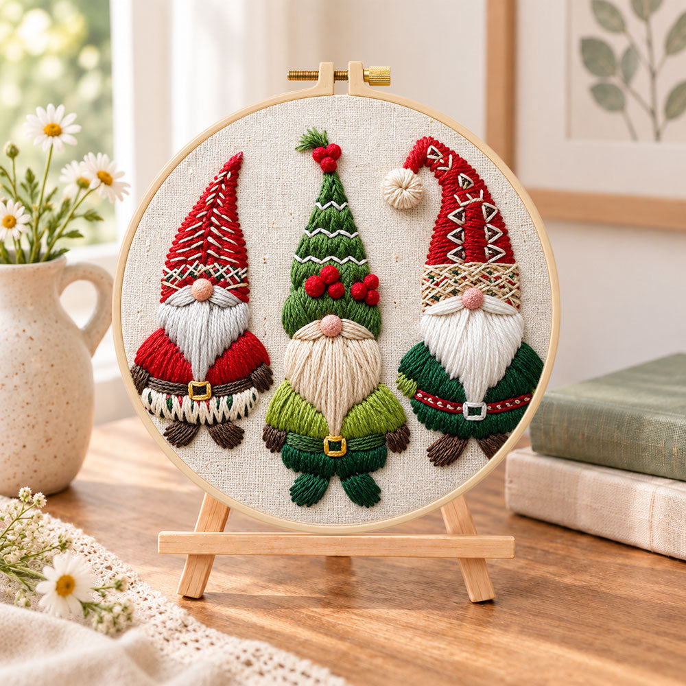 Three christmas gnomes embroidery kit finished hoop displayed on a wooden stand as cozy tabletop decor