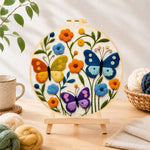 Finished three whimsical butterflies among flowers needle felting displayed on a wooden easel