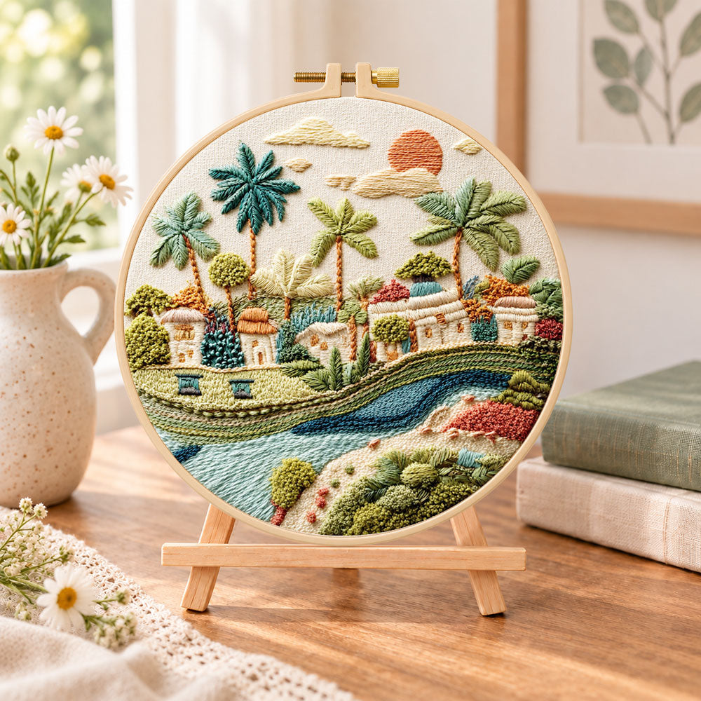 Tropical riverside hamlet embroidery kit finished hoop displayed on a wooden stand as cozy tabletop decor