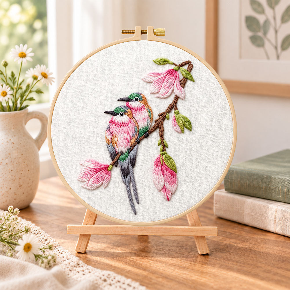 Two birds on magnolia branch embroidery kit finished hoop displayed on a wooden stand as cozy tabletop decor