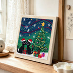 Two black cats under christmas tree punch needle artwork displayed on a table