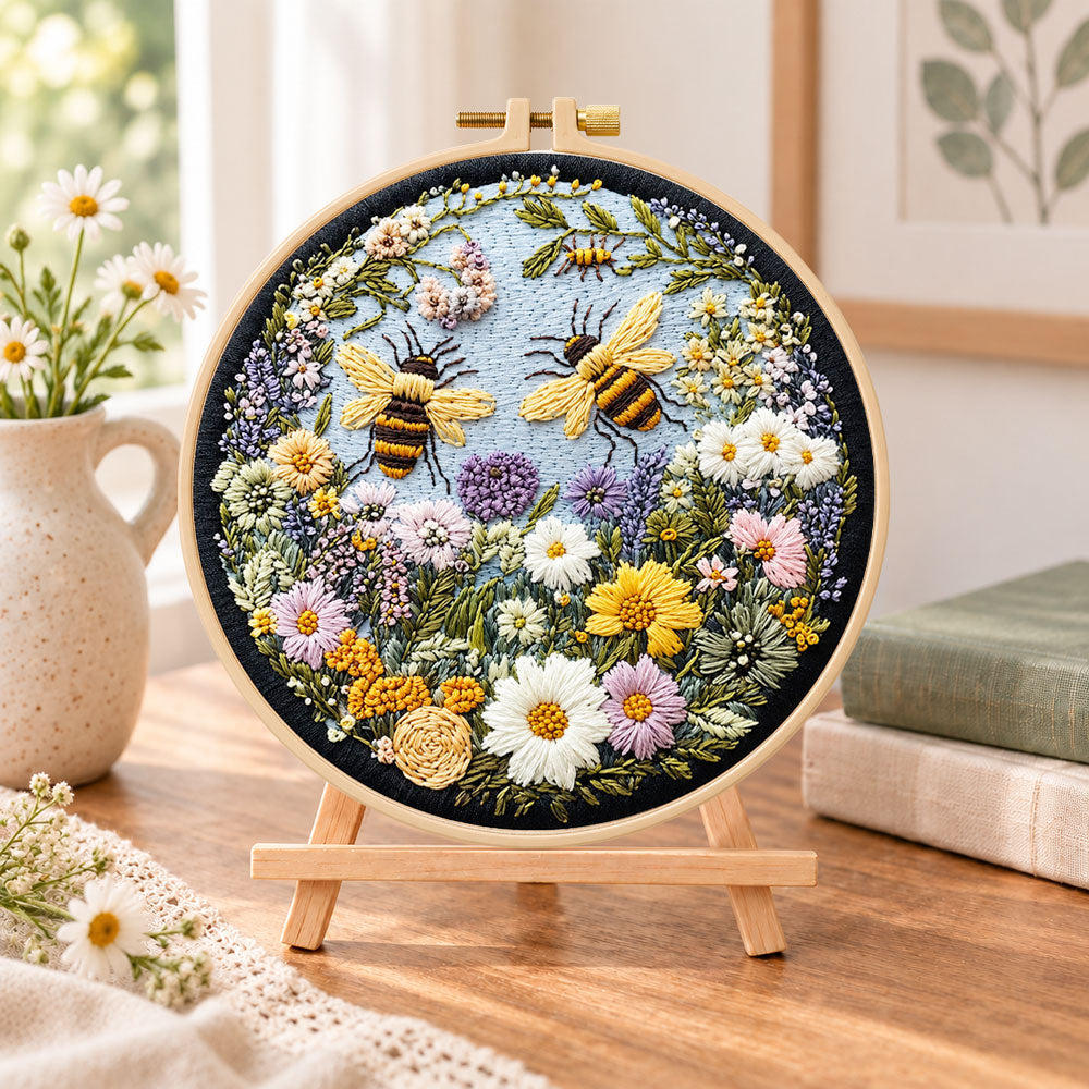 Two bumblebees in flower garden embroidery kit finished hoop displayed on a wooden stand as cozy tabletop decor