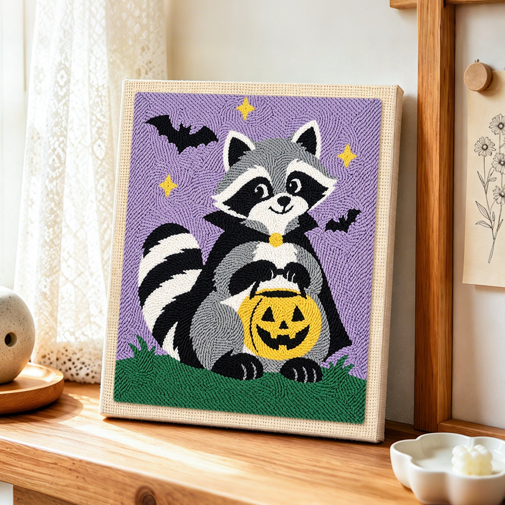 Vampire raccoon with pumpkin bucket punch needle artwork displayed on a table