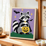 Vampire raccoon with pumpkin bucket punch needle artwork displayed on a table
