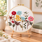 Vibrant mixed blooms embroidery kit finished hoop displayed on a wooden stand as cozy tabletop decor