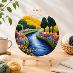 Finished vibrant rolling hills, sunny river and rainbow flowers needle felting displayed on a wooden easel