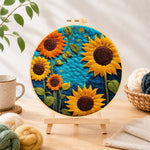 Finished vibrant sunflowers on blue needle felting displayed on a wooden easel