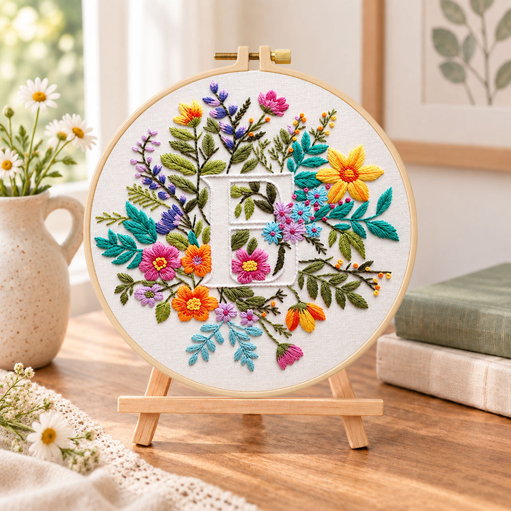 Vibrant wildflowers and letter e embroidery kit finished hoop displayed on a wooden stand as cozy tabletop decor