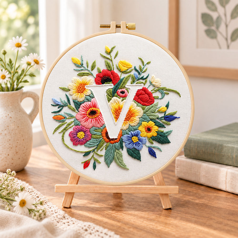 Vibrant wildflowers and letter v embroidery kit finished hoop displayed on a wooden stand as cozy tabletop decor