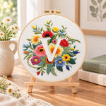 Vibrant wildflowers and letter v embroidery kit finished hoop displayed on a wooden stand as cozy tabletop decor