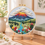 Volcanic mountain view embroidery kit finished hoop displayed on a wooden stand as cozy tabletop decor