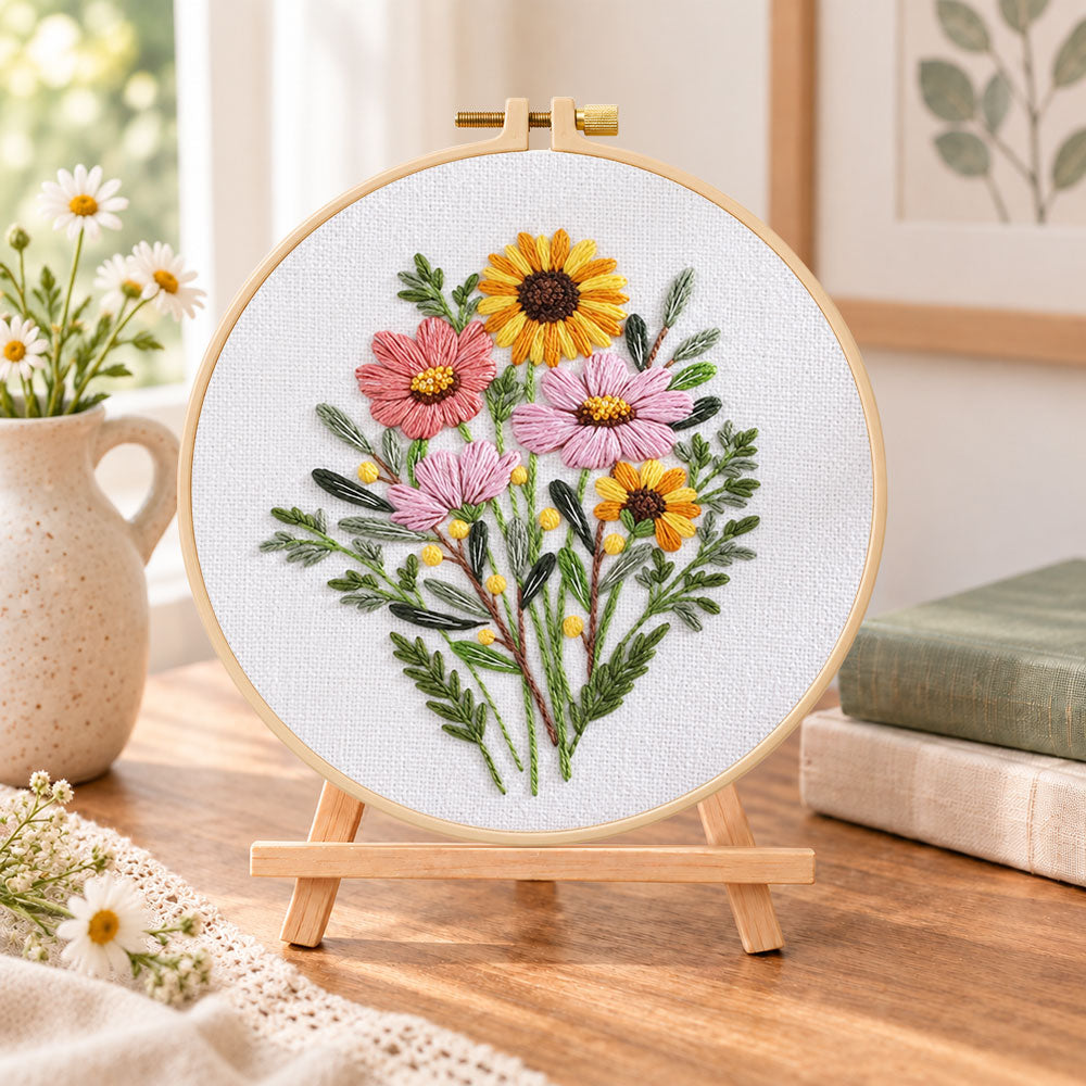 Warm‑toned posy embroidery kit finished hoop displayed on a wooden stand as cozy tabletop decor