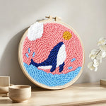 Whale jumping in pink sky punch needle artwork displayed on a table