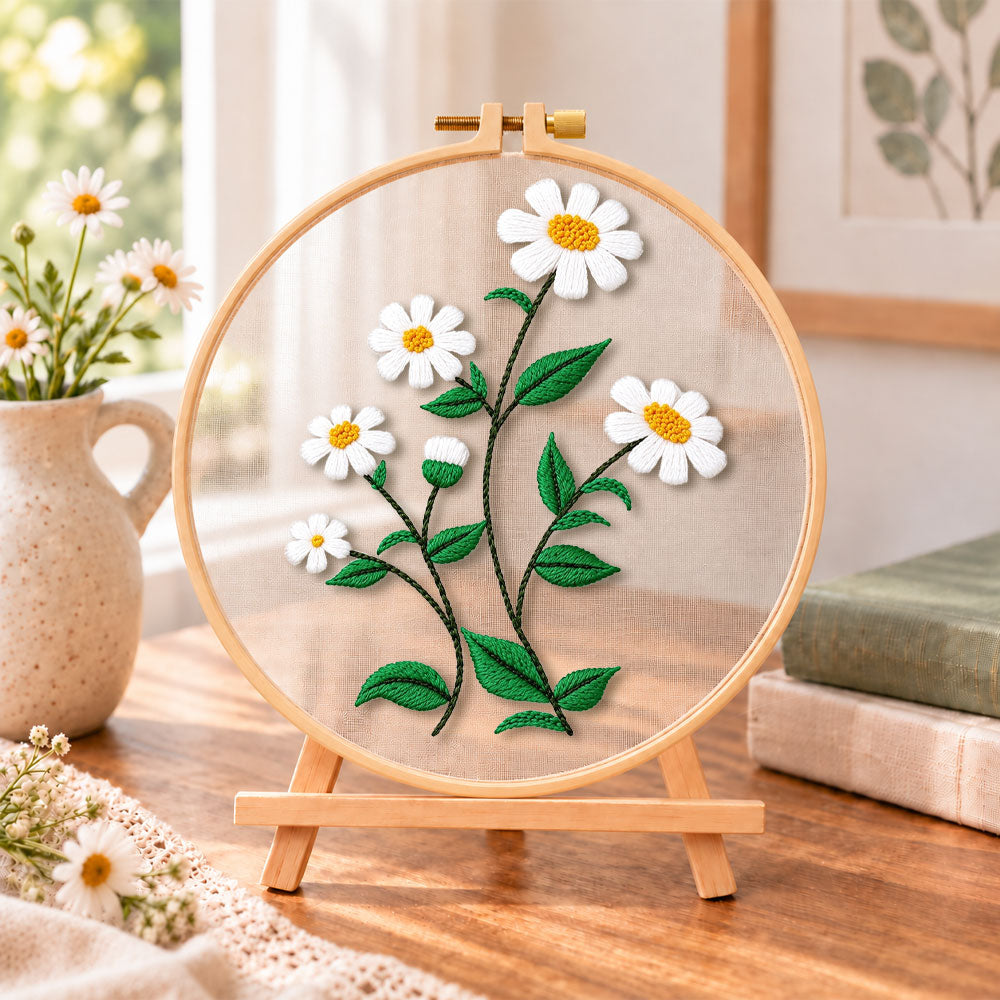 White daisies with green leaves embroidery kit finished hoop displayed on a wooden stand as cozy tabletop decor
