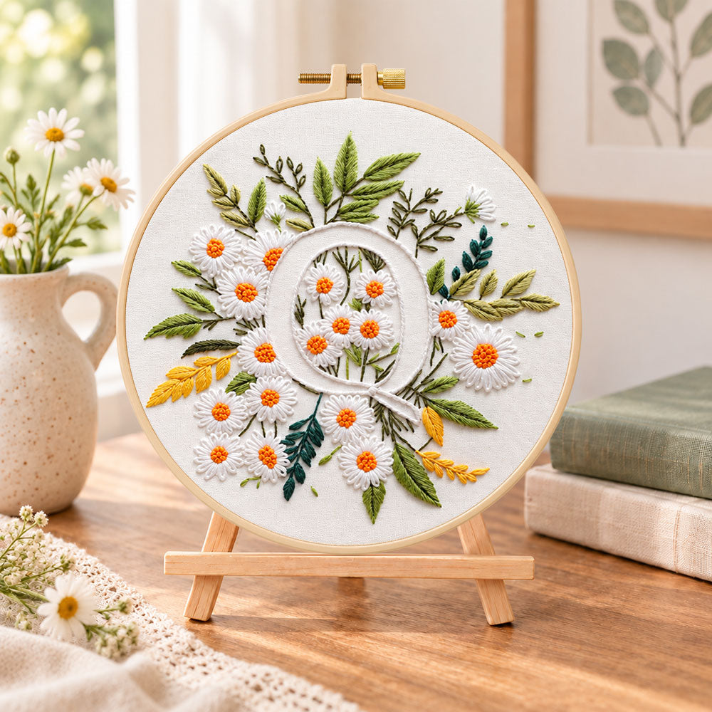 White daisy cluster and letter q embroidery kit finished hoop displayed on a wooden stand as cozy tabletop decor