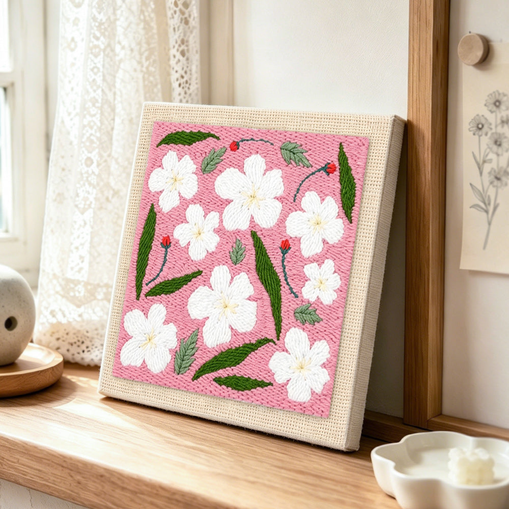 White flowers with green leaves punch needle artwork displayed on a table