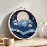 White moon above blue snowy mountains punch needle artwork displayed on a table