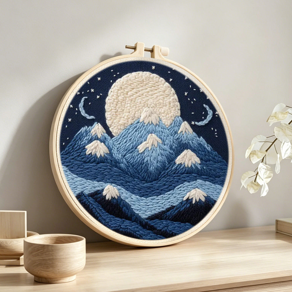 White moon above blue snowy mountains punch needle artwork displayed on a table