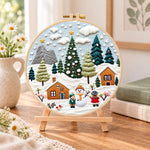 Winter snowy village embroidery kit finished hoop displayed on a wooden stand as cozy tabletop decor