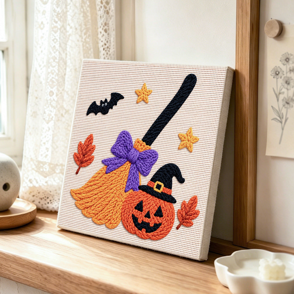 Witch broom and jack‑o‑lantern punch needle artwork displayed on a table