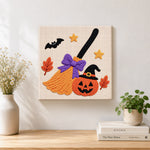 Finished witch broom and jack‑o‑lantern artwork displayed on a wall