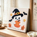 Witch ghost holding pumpkin punch needle artwork displayed on a table