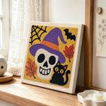 Witch hat skull and black cat punch needle artwork displayed on a table