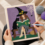 Creating handmade witch reading beside black cat punch needle artwork