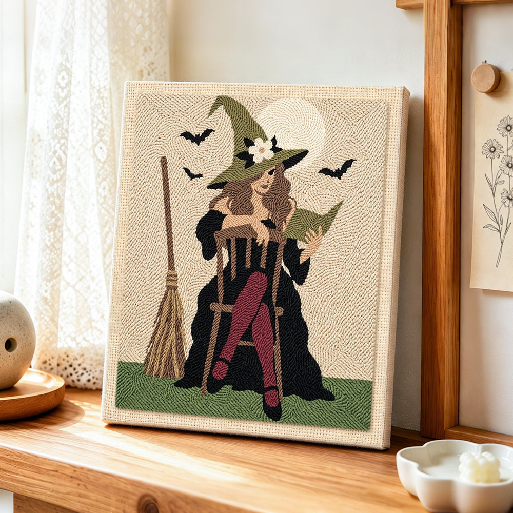 Witch seated with spell book punch needle artwork displayed on a table