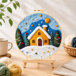 Finished yellow snowy cottage at christmas needle felting displayed on a wooden easel