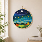 Yellow tower house and rolling green clouds needle felt wall art displayed in a bright home interior